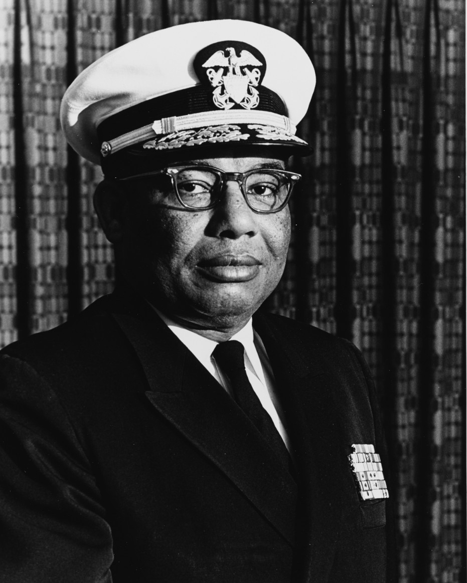 A black and white photograph of an African American man with glasses in formal Navy blue uniform. 