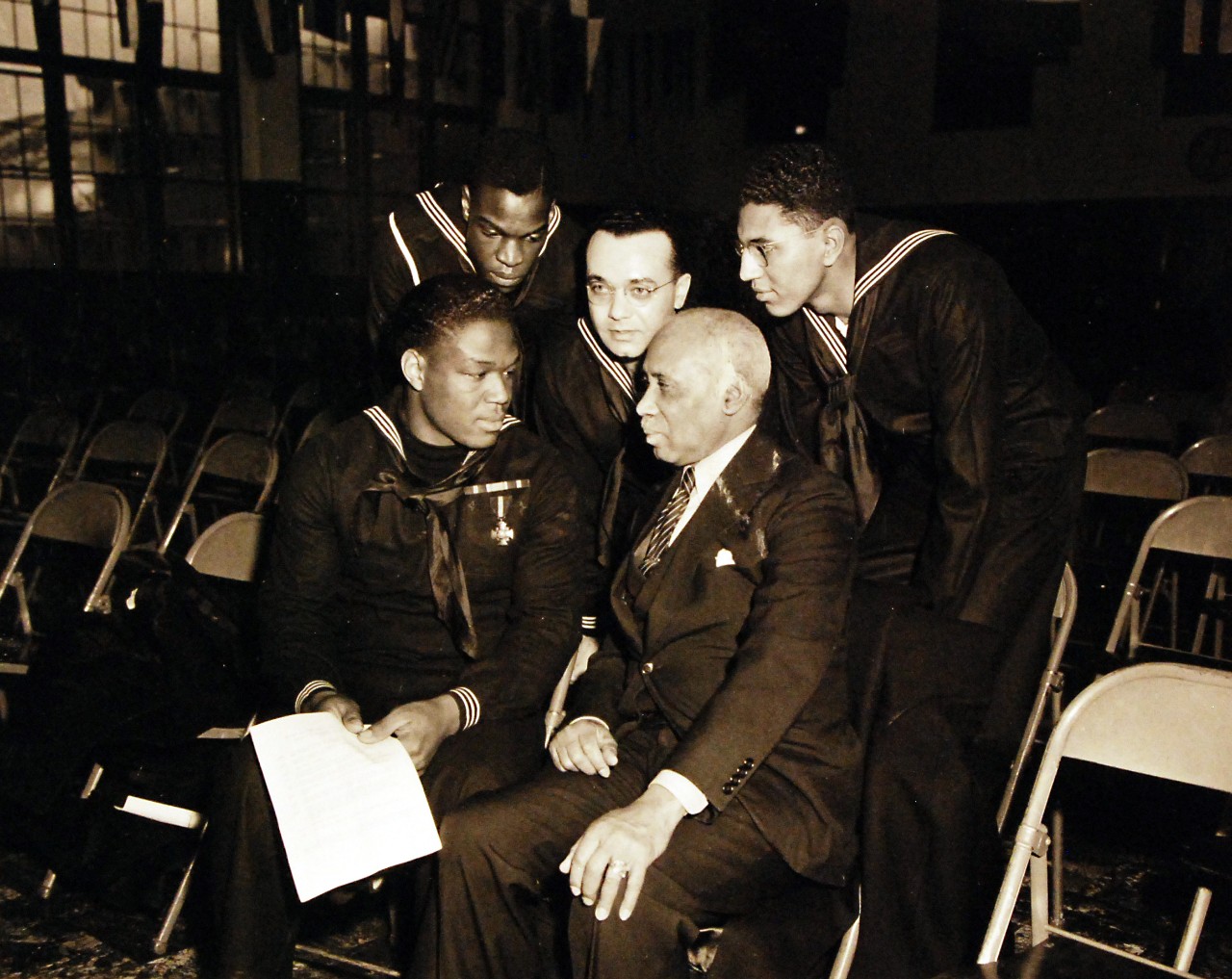 80-G-294804:  Doris Miller, Mess Attendant First Class, USN.  Talking with three other sailors and a civilian, during his visit to the Naval Training Station, Great Lakes, Illinois, 7 January 1943.  He is wearing the Navy Cross medal, awarded for heroism during the Pearl Harbor Attack, 7 December 1941.  Official U.S. Navy Photograph, now in the collections of the National Archives.  Also at NHHC.  (2016/07/05). 