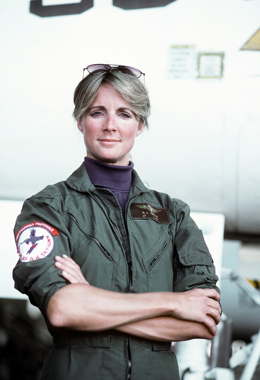 A woman stands with arms crossed in front of an aircraft. 