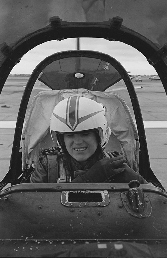 A woman seated in the cockpit of a training aircraft.