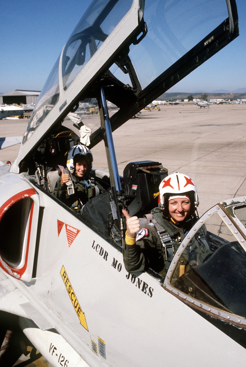 Two women seated in the cockpit of a plane, both indicating with a thumbs-up. 