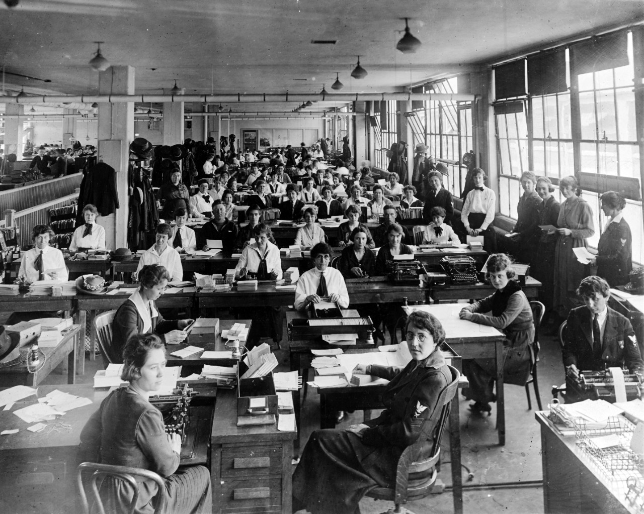 Long view of a building interior with personnel sitting at desks and standing. 