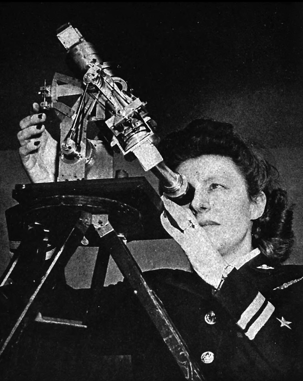 A woman in blue Navy uniform looking through a sextant.