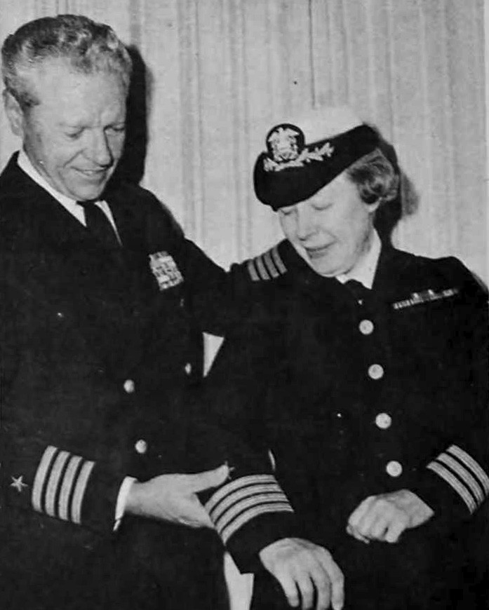 Man in uniform adds stripe to uniform of a woman in uniform. 
