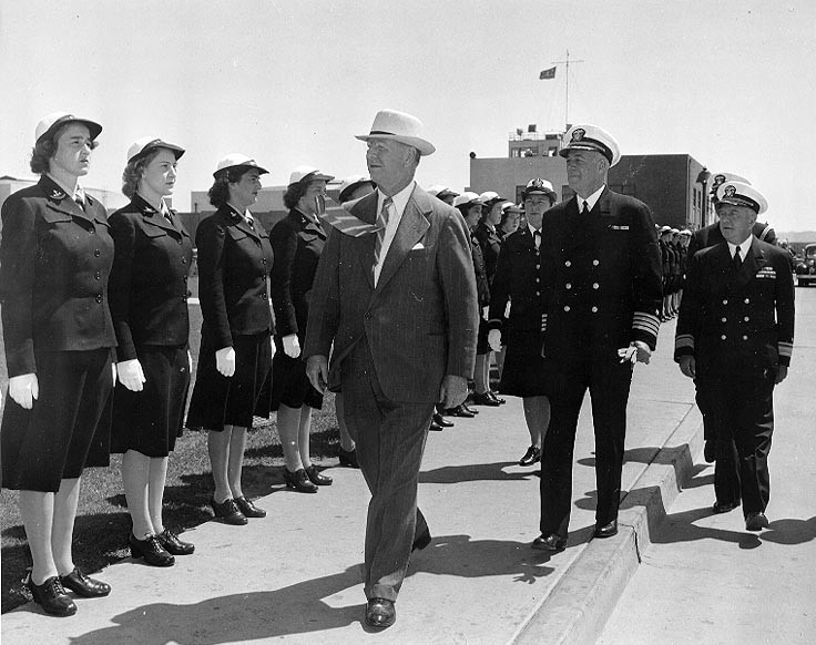 Women in uniform stand at attention as a man in civilian clothes and two officers in uniform look them over.