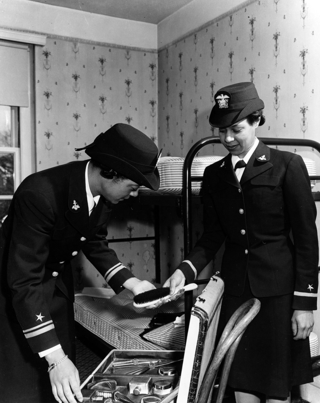 One female officer hands another a brush to pack in a suitcase