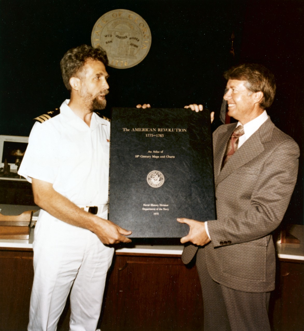 Photo of two men standing holding a large book between them. 