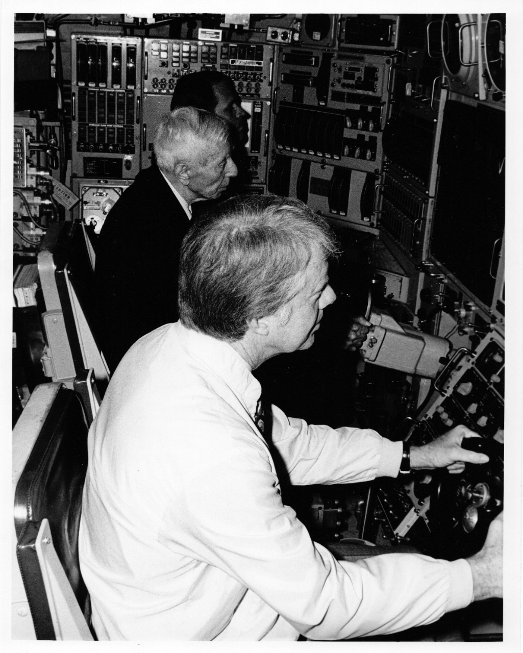 Black and white photograph of President Jimmy Carter at a control panel aboard a submarine.  and Admiral Rickover 