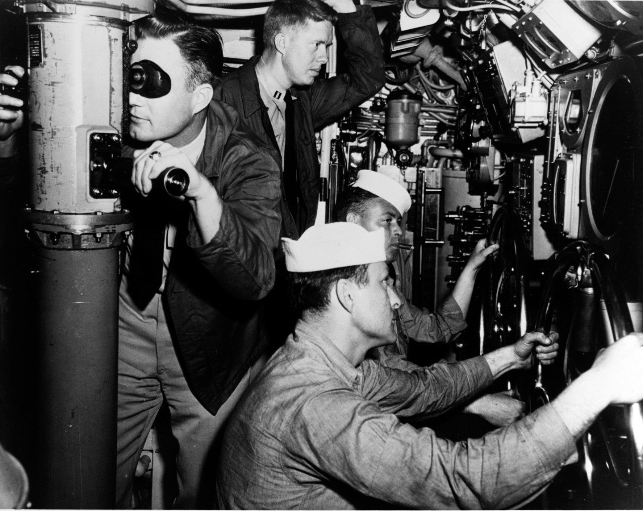 Black and white photograph of four men working in close quarters on a Navy submarine. 