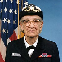 <p>A portrait of a white woman in naval uniform with cover, U.S. flag in background.&nbsp;</p>
