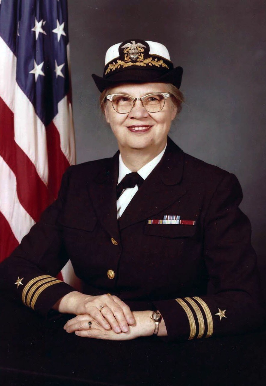<p>Official portrait of Commander Toms in uniform of the Naval Reserve with the American flag in background</p>