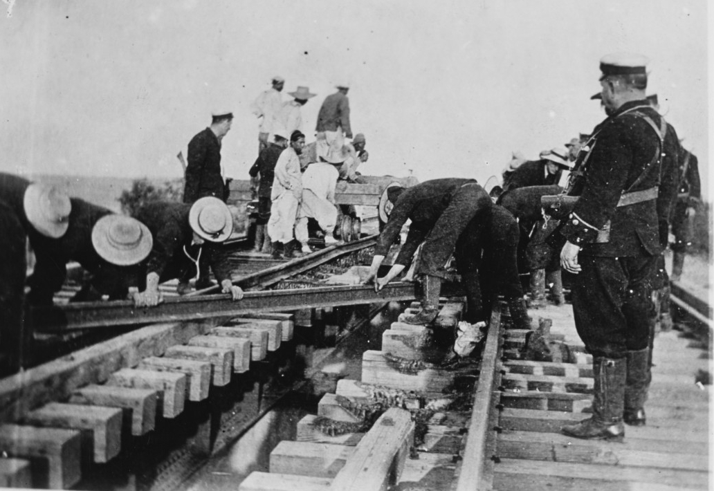 Men laying down railroad track. Clicking this linked image leads to a page where the photograph can be downloaded.