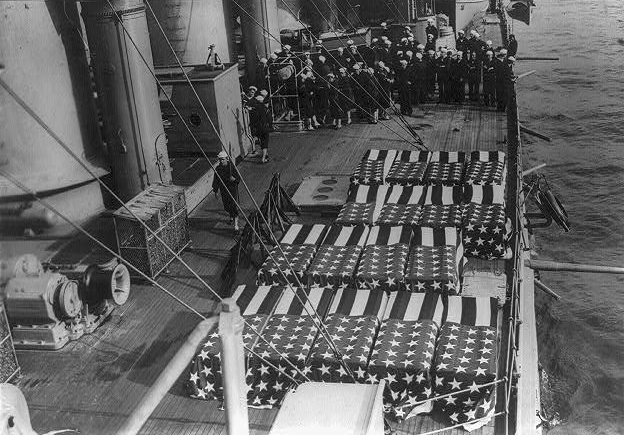 Caskets covered with the American flag on a ship's deck.