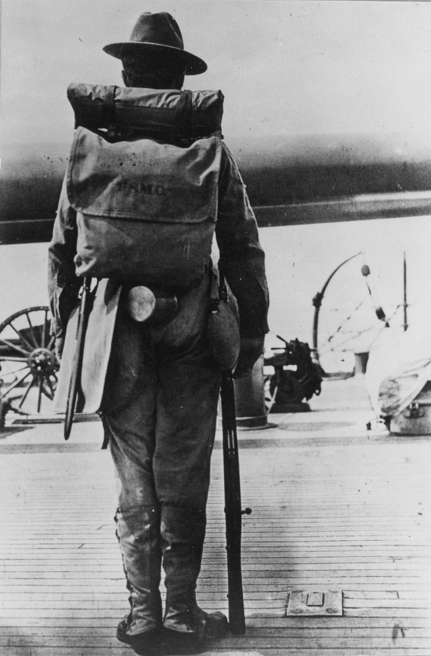 A marine wearing a pack on his back and holding a rifle.
