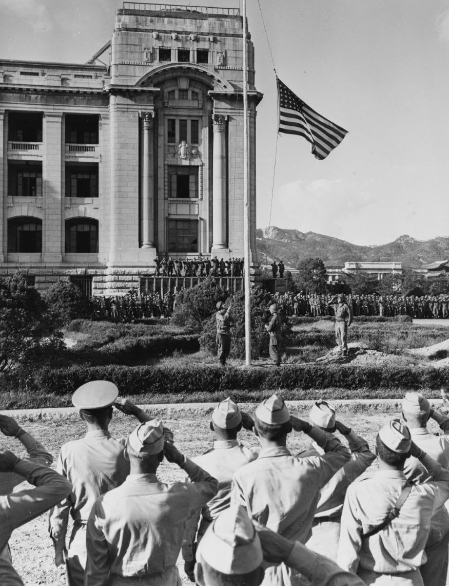 Lowering the Japanese flag attended by a large crowd of uniformed personnel in front of a government building