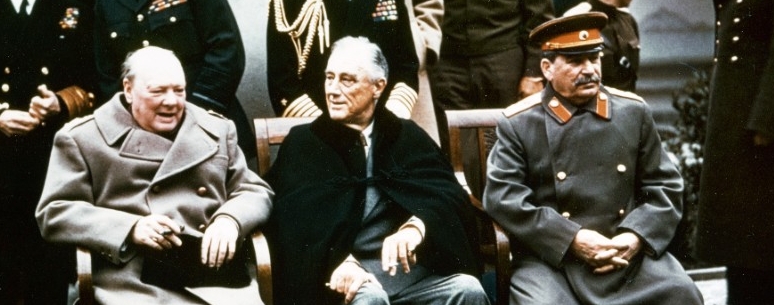The three leaders at Yalta seated in front of a crowd of aides standing behind them