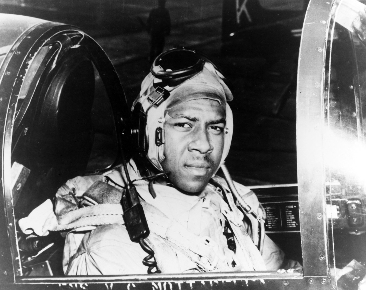 Photo of African American man in a Navy flight suit staring at the camera from the cockpit of his airplane.
