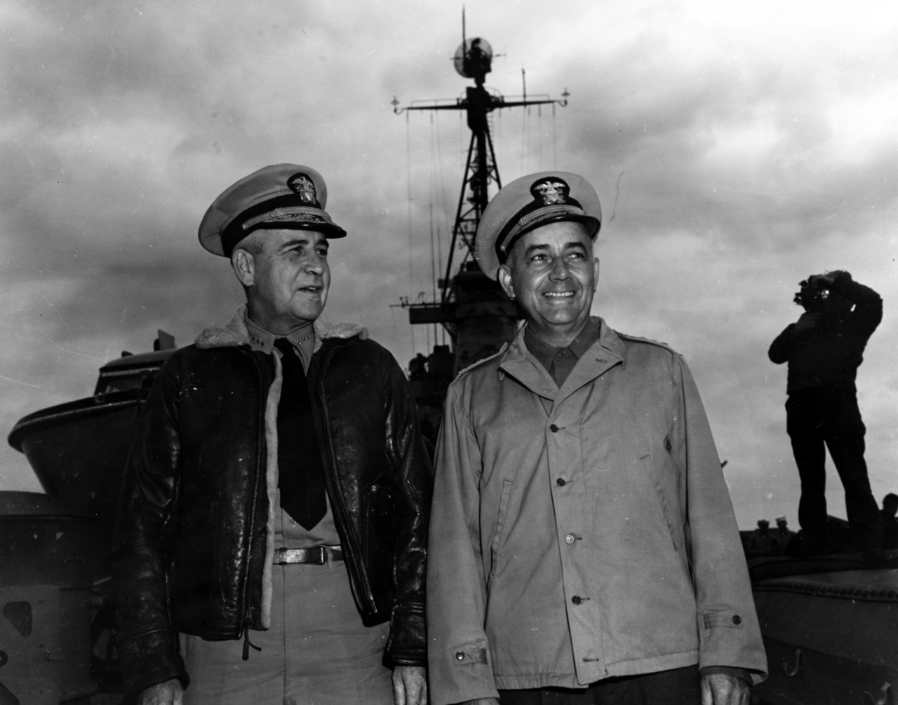 Two men standing on the deck of a battleship in their uniforms smiling.