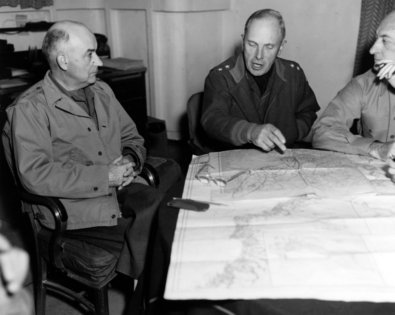 3 unformed men sit around a table, one pointing at map in front of them