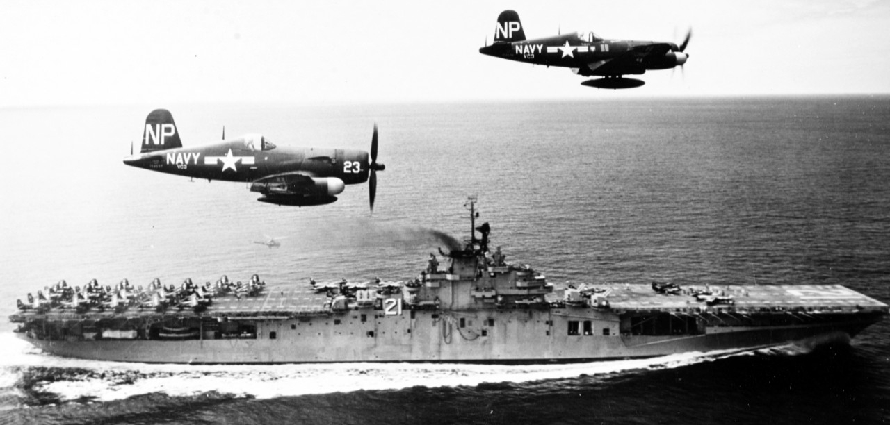 Aircraft carrier underway with two Corsair aircraft escorts.