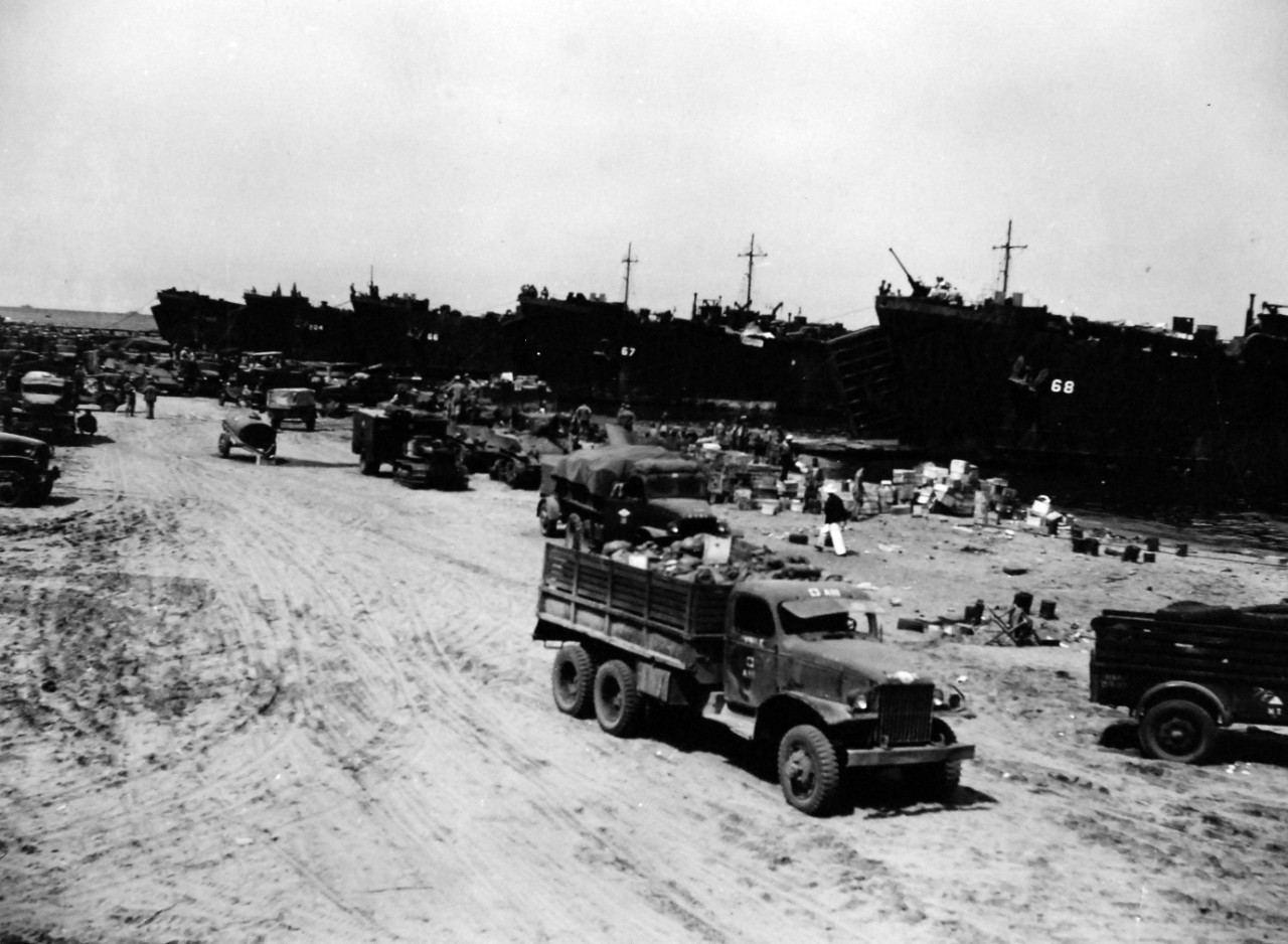 80-G-57458: Battle of Cape Gloucester, New Britain, December 1943-January 1944. Supplies being unloaded on the beachhead by LST-66, LST-67, LST-68, LST-202, and LST-204. Photographed by USS Nashville (CL-43), December 24-26, 1943. 