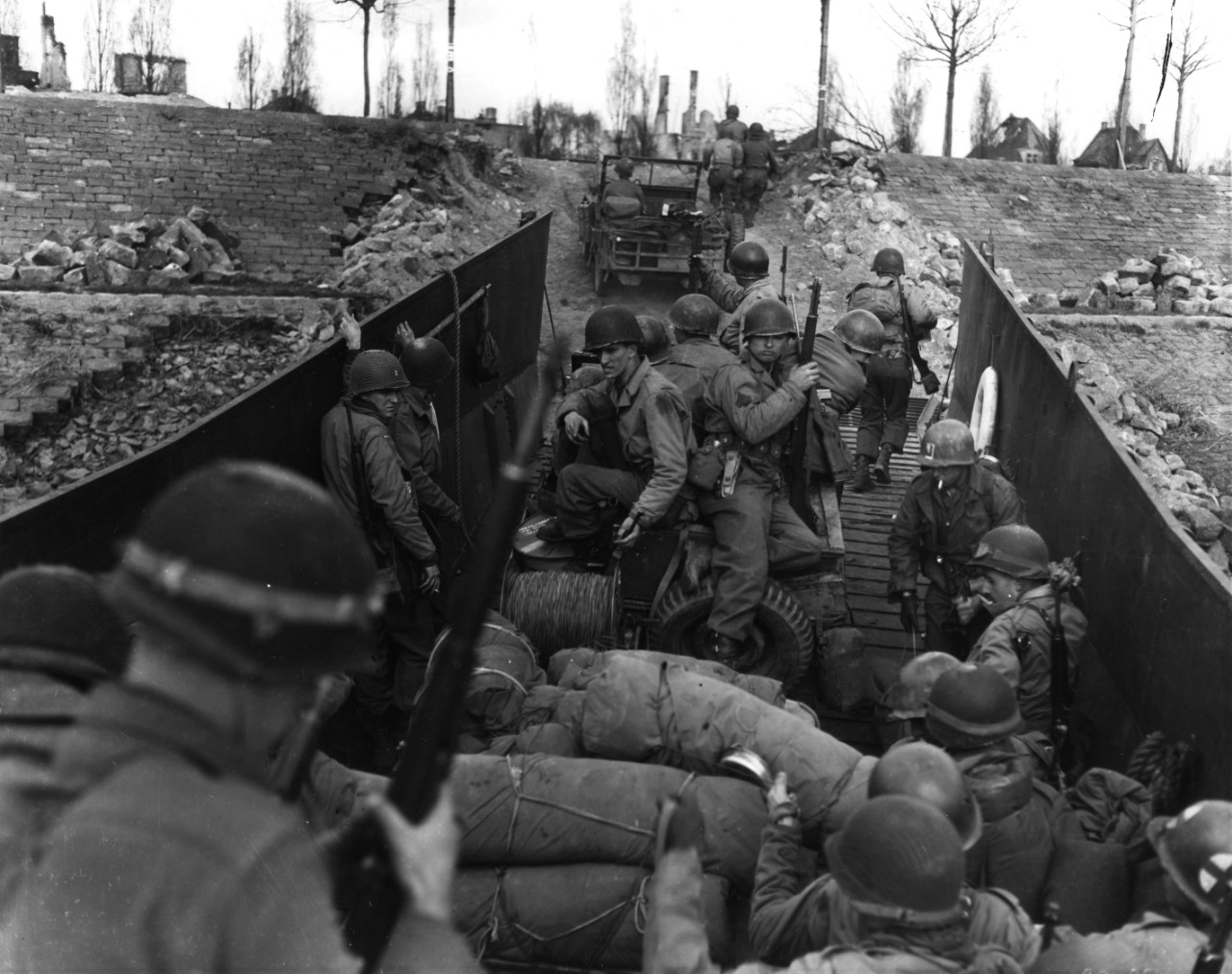 Men and vehicles of the 80th Infantry Division, Third US Army, load into a landing craft prior to crossing the Rhine River, Germany, 29 March 1945. Note M-1 Garand rifle and belt gear of man in center, including TL-29 knife, and M-1 carbines carr...