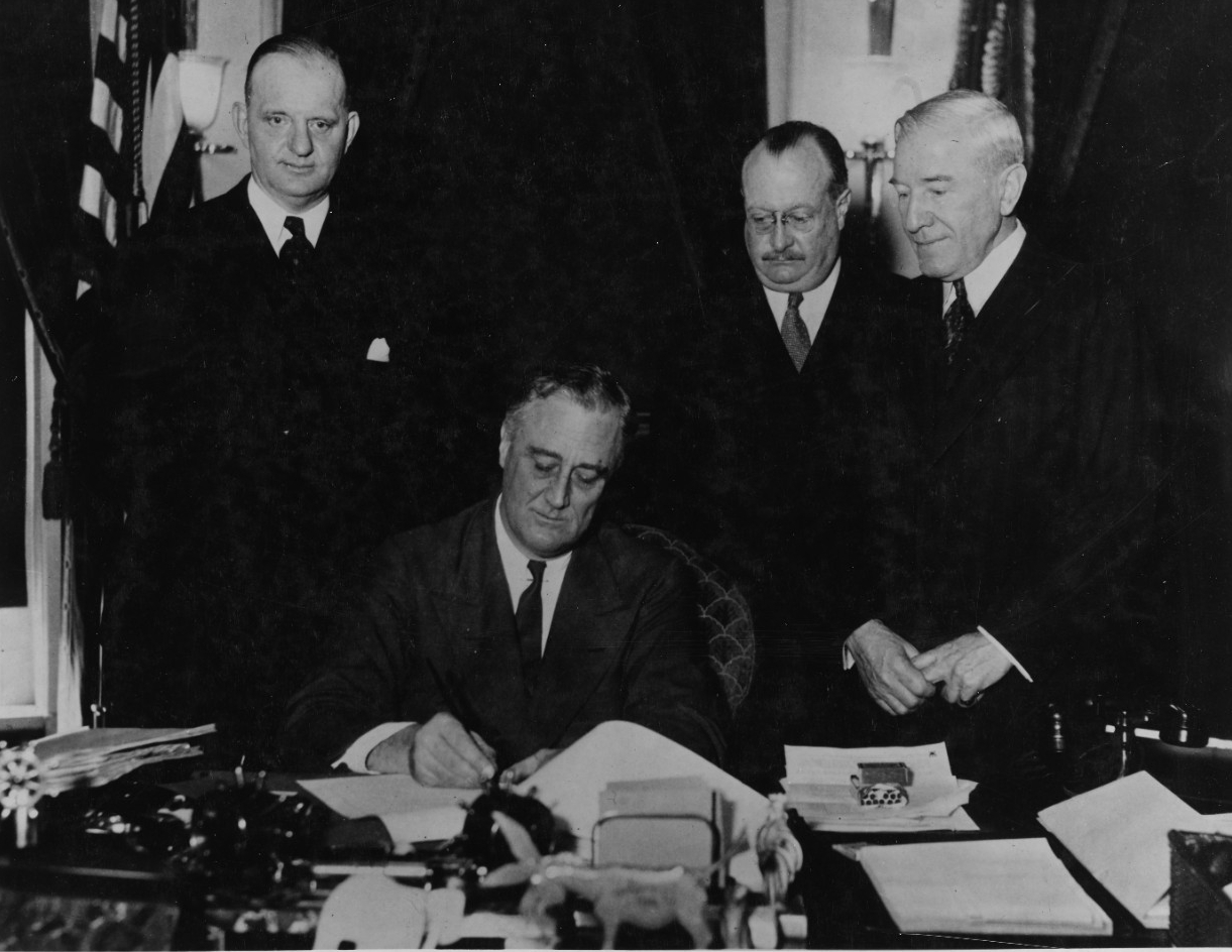 President Franklin D. Roosevelt (center) signs the 1934 Vinson-Trammell Act, which allowed an increase in shipbuilding within treaty limits. Peacetime legislation, along with Roosevelt’s strong advocacy for ship construction, primed the United St...