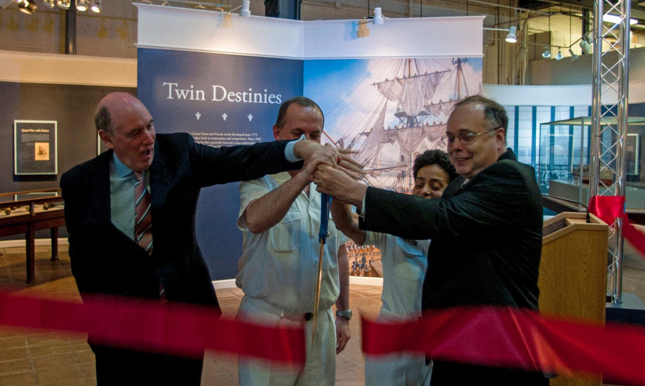 <p>Director, Naval History and Heritage Command, Rear Adm. Sam Cox (Ret.) (right), Vice Chief of Naval Operations Adm. Michelle Howard (center right), French Rear Adm. Hervé Bléjean (center left), and Miles Young, president of Friends of L'Hermione-Lafayette in America (left), cut the ceremonial ribbon opening the exhibit “Twin Destinies” to the public, in the National Museum of the United States Navy, June 8, 2015. Twin Destinies showcases the partnership between the American and French navies from the creation of the country to the present. (U.S. Navy photo by Mass Communication Specialist 2nd Class Eric Lockwood/Released)</p>
