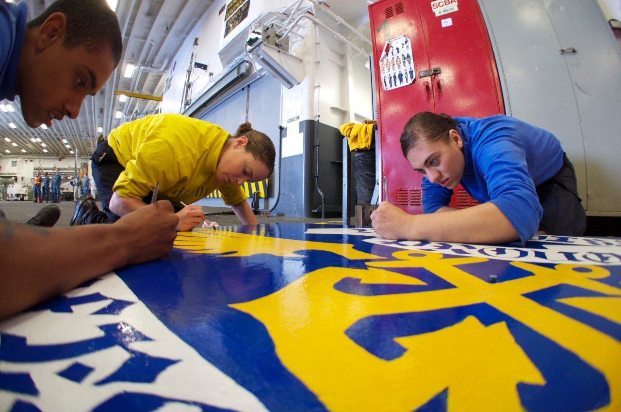 Sailors assigned to V3 division aboard the amphibious assault ship USS Bonhomme Richard (LHD 6) finish painting a sign with their motto of Proud, Professional.