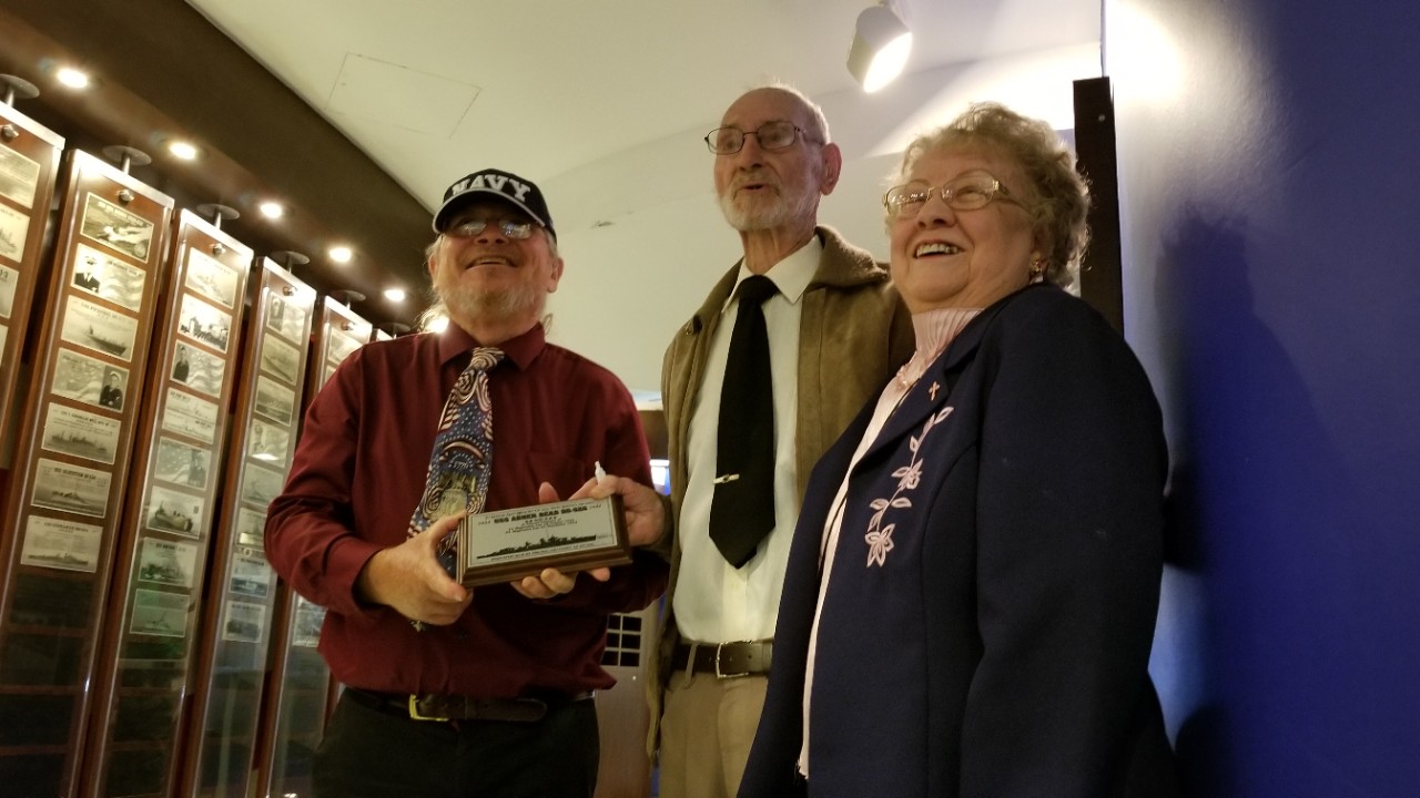 Three people hold the plaque of the USS Abner Read dedication ceremony 