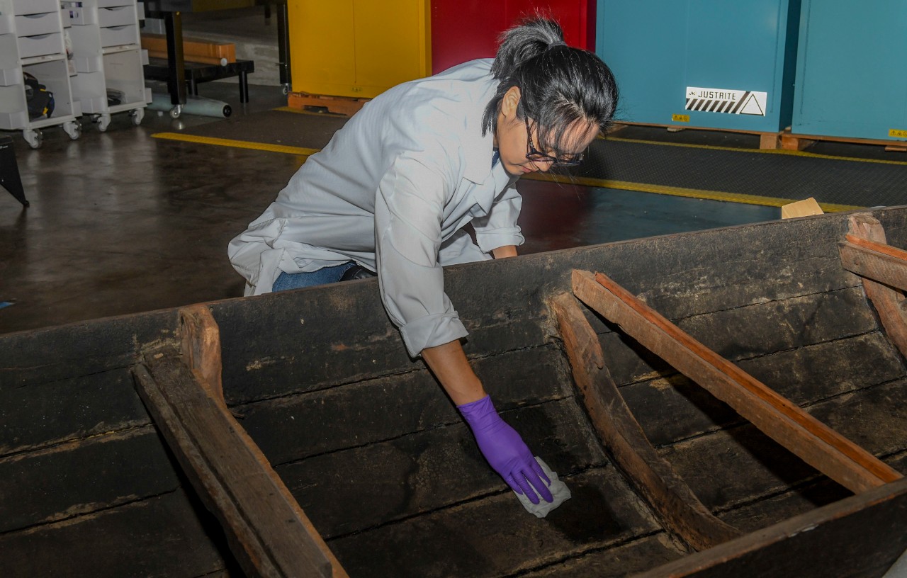 Yoonjo Lee, senior conservator deputy at the Conservation Branch, Collection Management Facility, Naval History and Heritage Command, uses distilled water to clean the planks of a Vietnamese watercraft called a sampan.