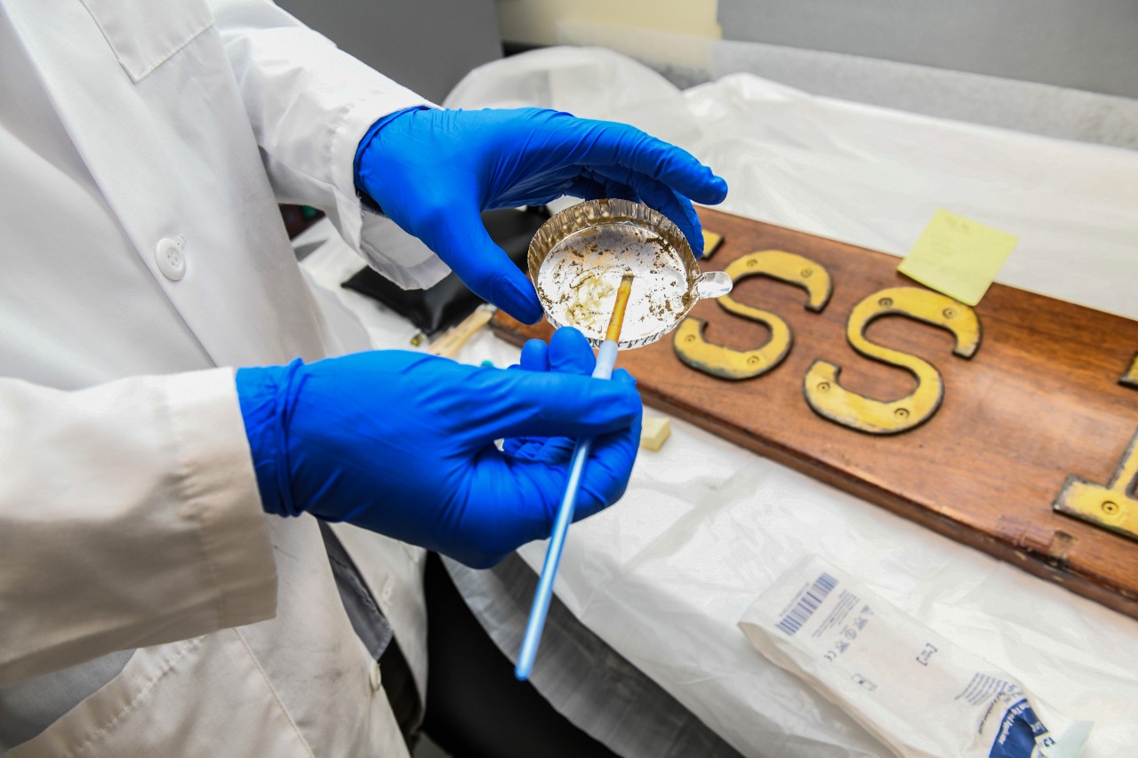 <p>Karl Knauer, a conservator at Collection Management Facility, Naval History and Heritage Command, applies a customized compound to halt the deterioration of a name plaque from the USS Enterprise (CVN 65).</p>