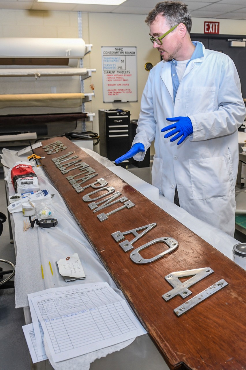 Karl Knauer, a conservator at Collection Management Facility, Naval History and Heritage Command, applies a customized compound to halt the deterioration of a name plaque from the USS Enterprise (CVN 65).