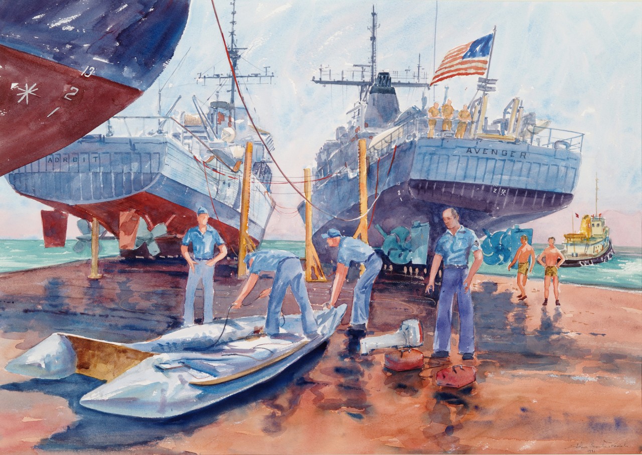 Navy crewmen work on an inflatable zodiac on the deck of a transport ship, with smaller ships on deck in the background