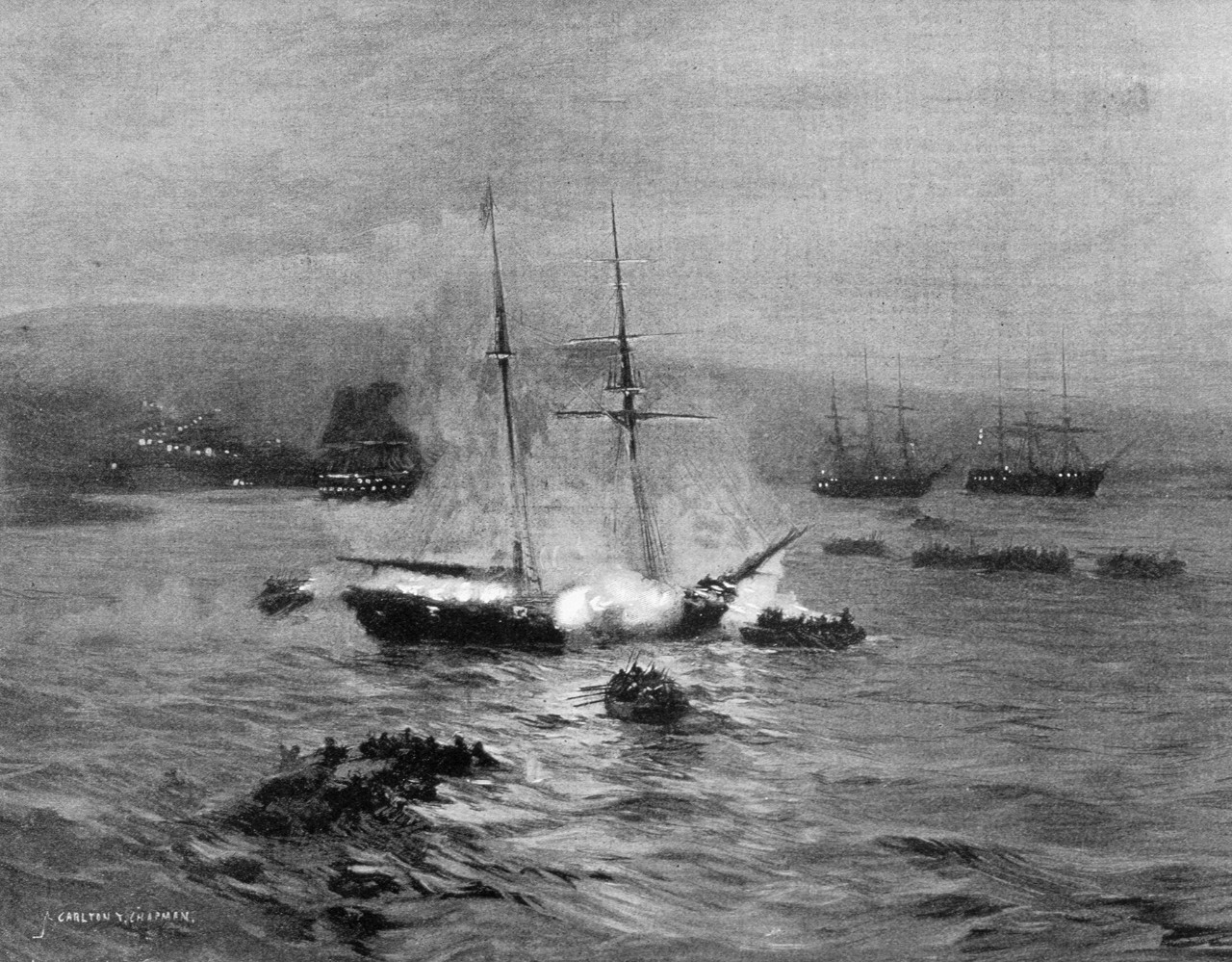 A ship is sinking with its deck on fire. The ship is surrounded by boats in the background are two large ships.