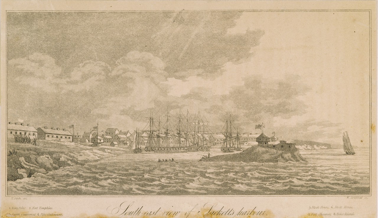 A view of a harbor with ships close to shore and buildings in the background. In the foreground is an island with a fort.