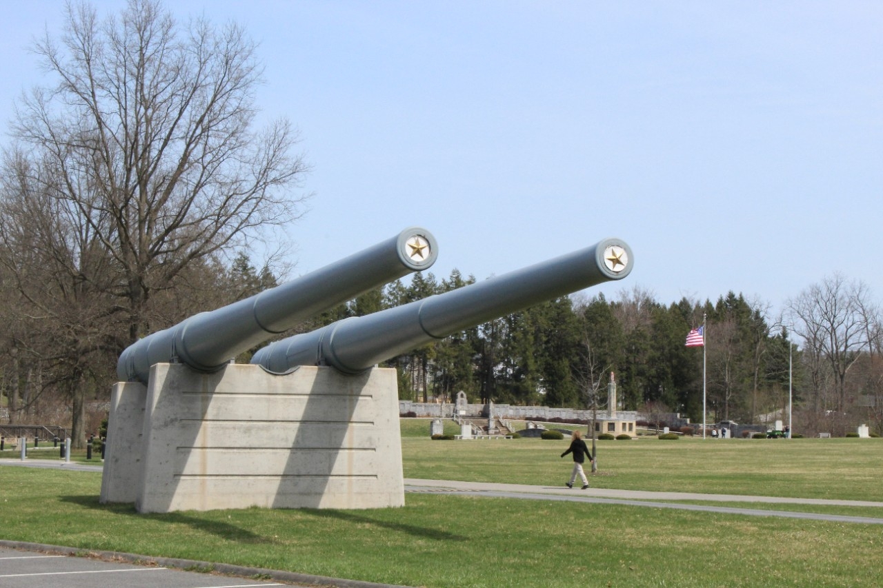 Two 14-inch/45 caliber gun barrels from USS Pennsylvania (BB-38). Both barrels are metal, painted gray, and mounted on two cement plinths. The exterior of the guns show three steps along their length and the barrels taper significantly towards th...
