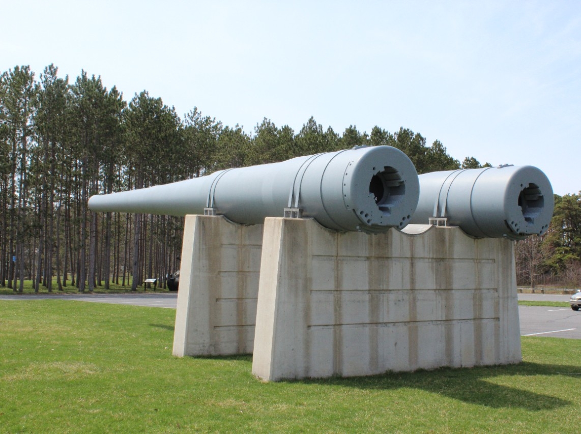 Rear view of two 14-inch/45 caliber gun barrels from USS Pennsylvania (BB-38). Both barrels are metal, painted gray, and mounted on two cement plinths. The exterior of the guns show three steps along their length and the barrels taper significant...