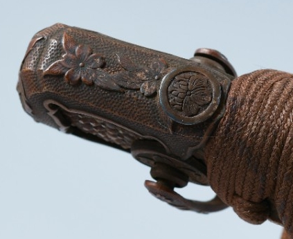A small metal disk on the front side of the pommel (kabuto-gane) decorated with a floral design.    