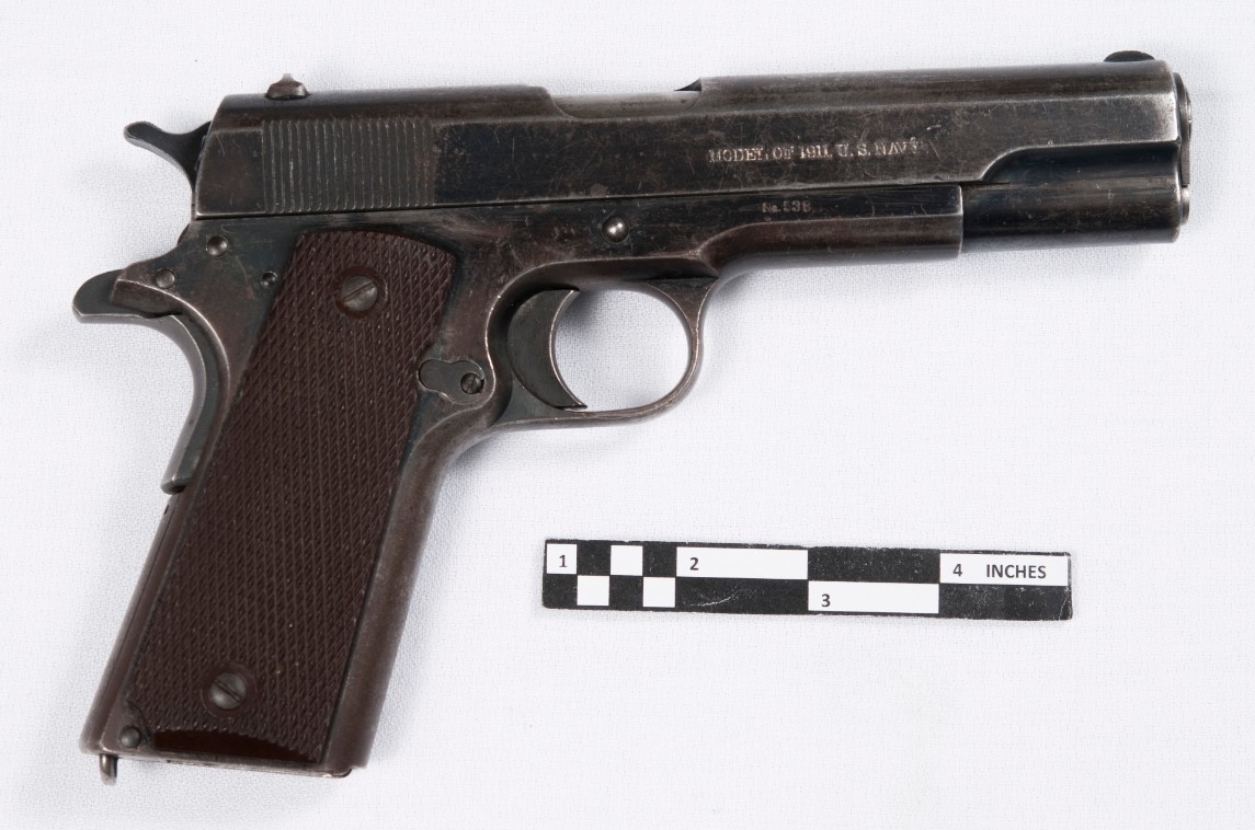 Obverse view of M1911 Navy pistol. .45 caliber pistol fed from 7-a 7-round detachable box magazine housed in the grip. Finish heavily worn from use. Checkered brown plastic grip. The obverse slide is marked “Model of 1911 U.S. Navy/No. 538.” 