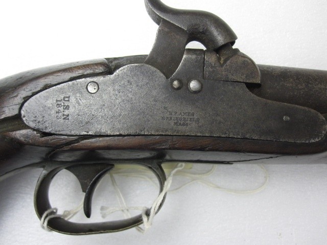 The lock plate is marked “U.S.N./1943” on the tail and “N.P.AMES/SPRINGFIELD/MA.” at the center below the hammer. The lock mechanism is entirely enclosed behind the plate, with only the hammer protruding from the top. A bolster with the percussio...