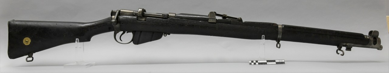 Right side of Lee-Enfield No. 1 Mk 3* Short Magazine rifle. Rifle has full-length dark wood stock with hooked semi-pistol grip. Metal triangular magazine loaded on underside of stock.