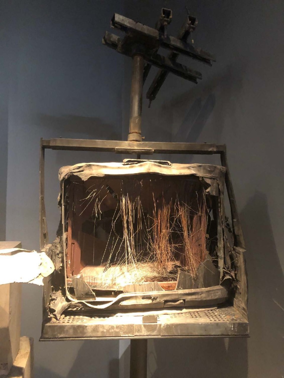 <p>Television on mounted wall/ceiling stand. Front glass broken out. Wires dangling inside. Covered in dust.</p>
