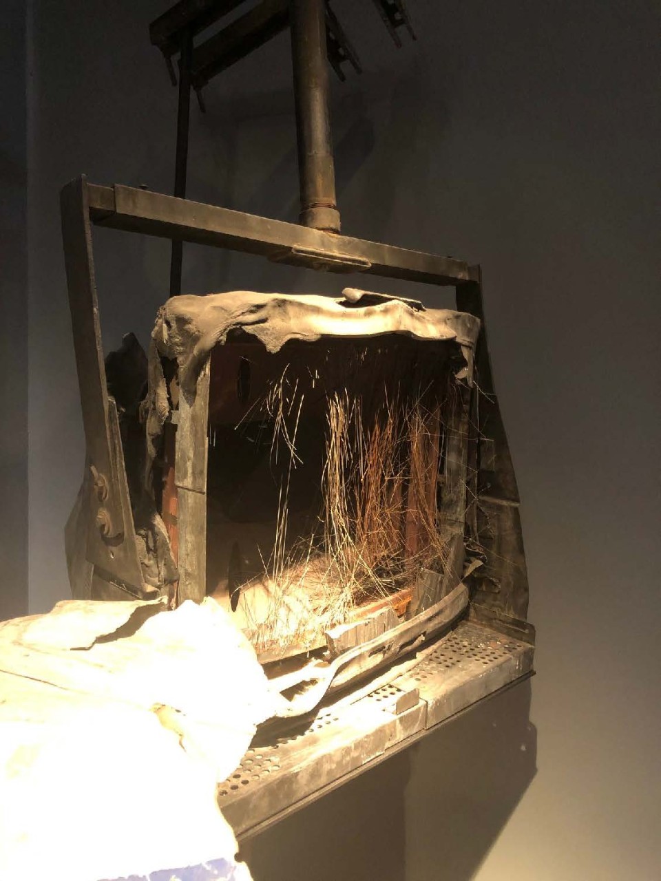 <p>Television on mounted wall/ceiling stand. Front glass broken out. Wires dangling inside. Covered in dust. Plastic case melted in places.</p>