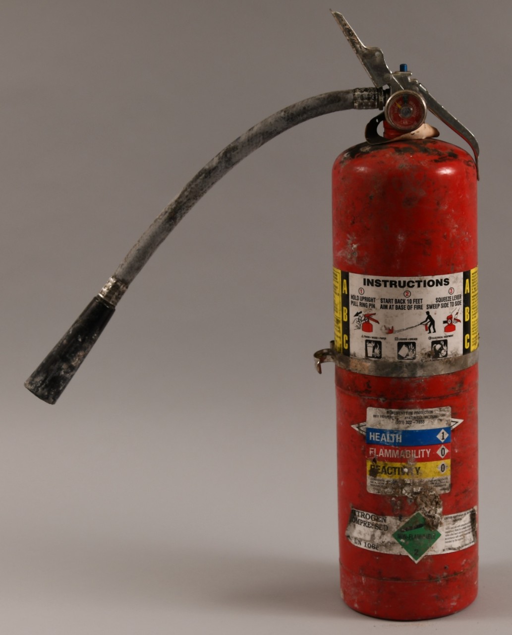 Reverse side of red fire extinguisher, hose extended to the left. Red pressuse gauge at top indicates it needs to be recharged.