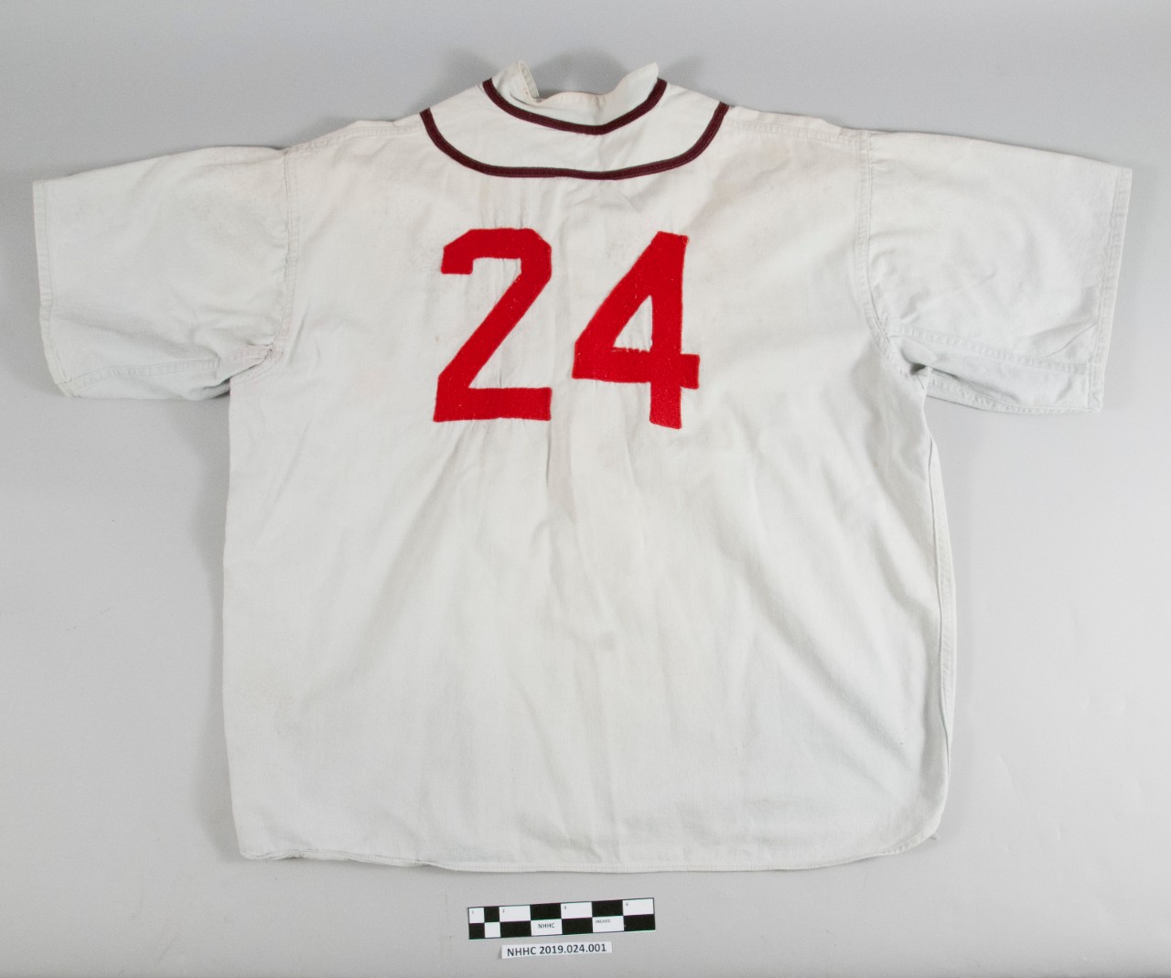 Reverse view of the baseball uniform blouse. Off-white in color with red lettering 24. Two brown stripes around the collar.