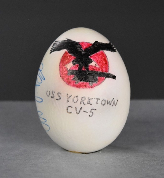 One egg, emptied of its contents, painted and signed. The egg is painted with an eagle with outstretched wings, gripping a cannon in its talons on a red field (the insignia of USS Yorktown), with USS Yorktown CV-5 written below it.