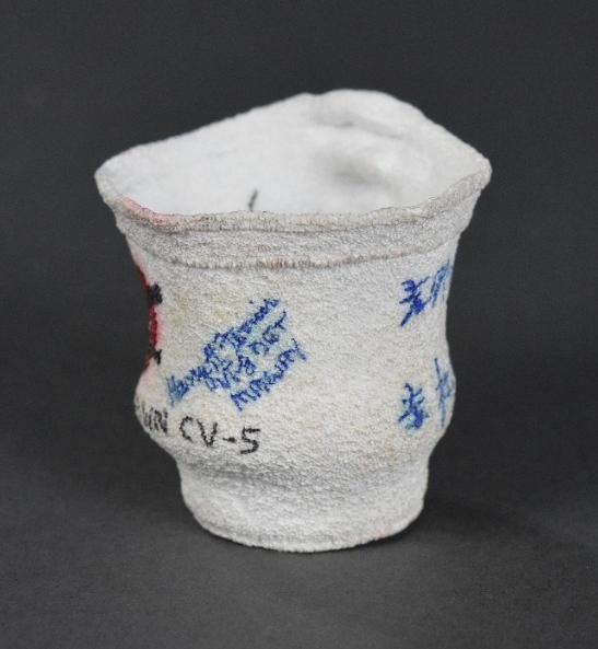 One crushed 8oz. Styrofoam coffee cup. It has a partial view of the USS Yorktown's insignia of an eagle carrying a cannon, with CV-5 written below it, and the signature of Harry H. Ferrier, VT-8 DET, Midway.