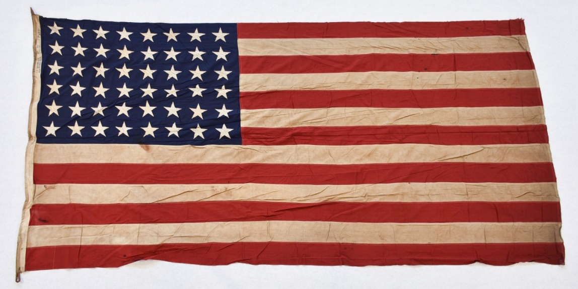 One forty-eight-star national ensign from the escort aircraft carrier USS Thetis Bay (CVE-90). The flag is cotton, of sewn construction and rectangular in shape. Seven alternating horizontal stripes of red and white are joined to a blue canton in...