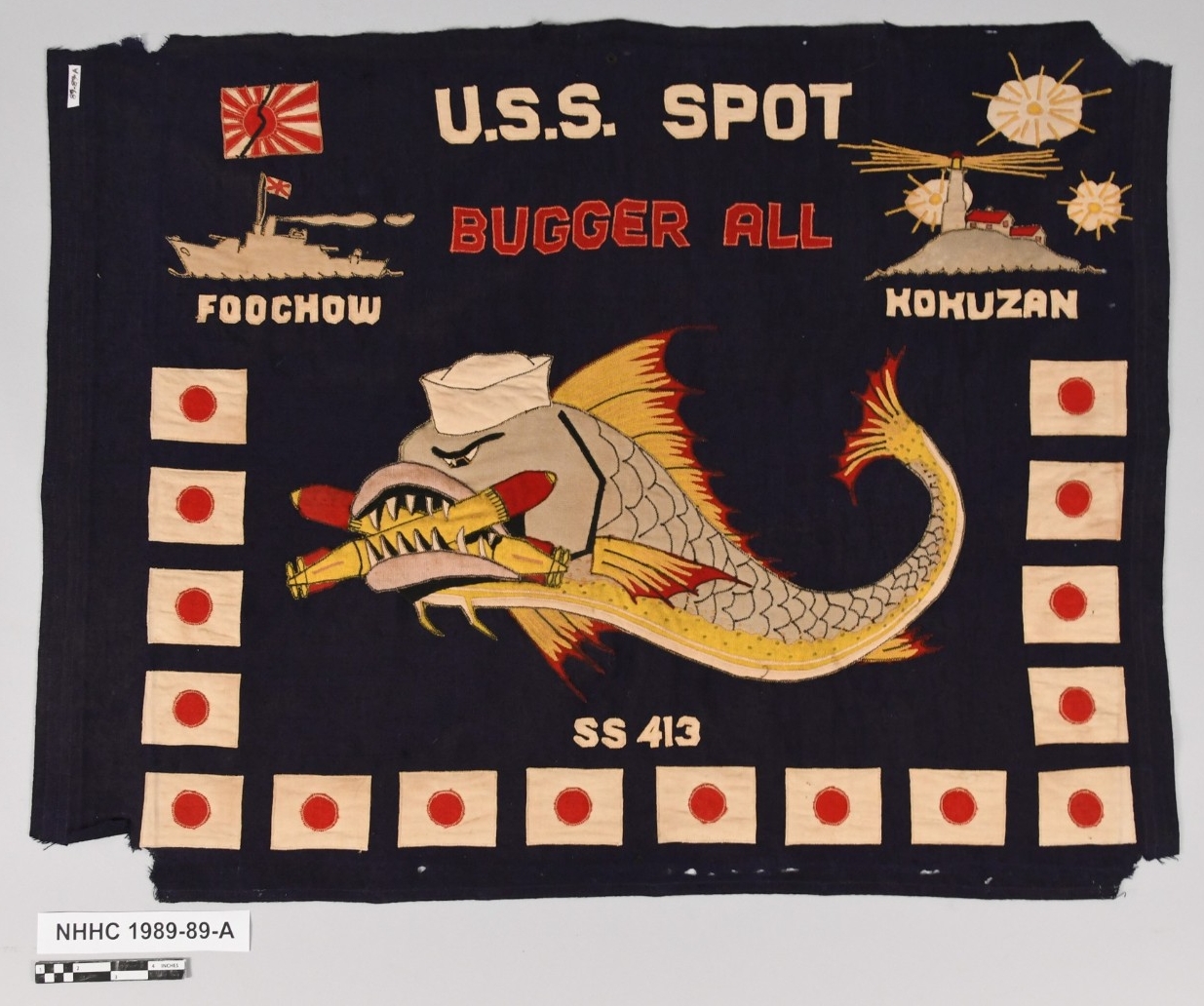 Navy blue battle flag with large fish insignia, sixteen Japanese flags, a Japanese ship, and and island sewn on.
